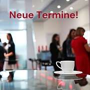 Eine Kaffeetasse steht auf einem Tisch, im Hintergrund sind Menschen.