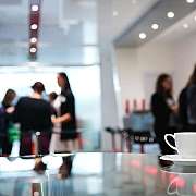 Eine Kaffeetasse steht auf einem Tisch, im Hintergrund sind Menschen.